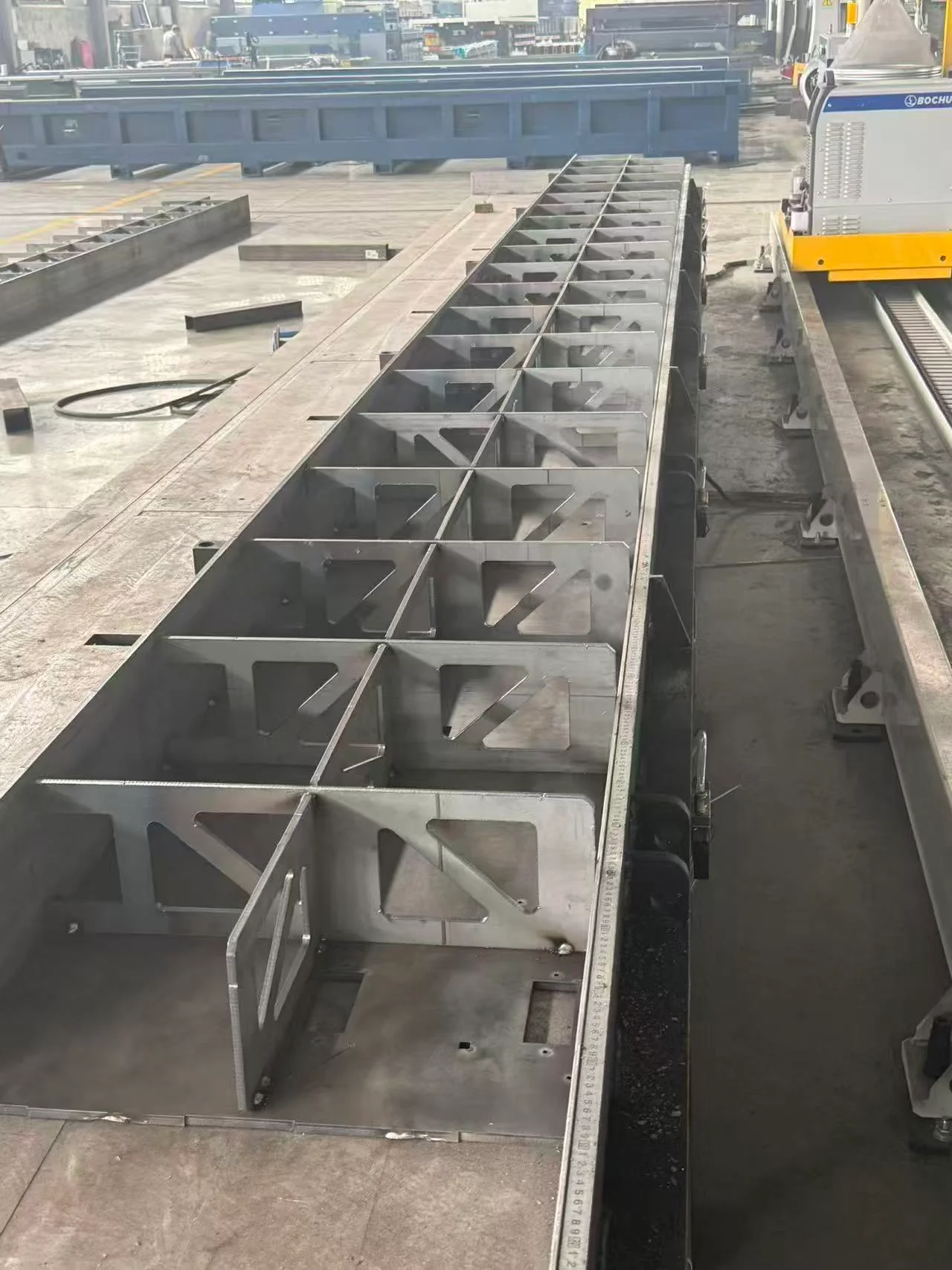 Long steel beam assembly with repeated stiffeners beside a BOCHU rail-mounted system.