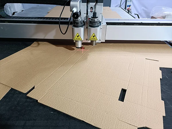 Digital cutting tools above a corrugated carton blank with cut tabs and fold lines; process reference