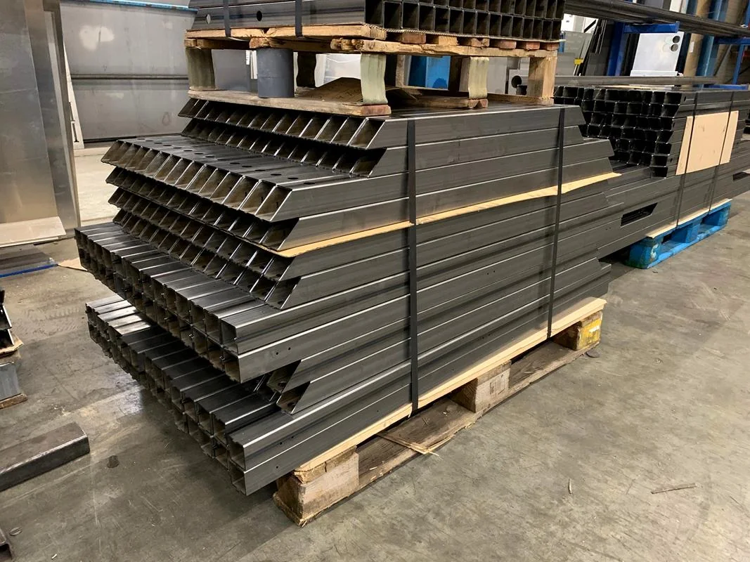 Cut rectangular steel profiles with connection holes stacked on pallets; industry reference