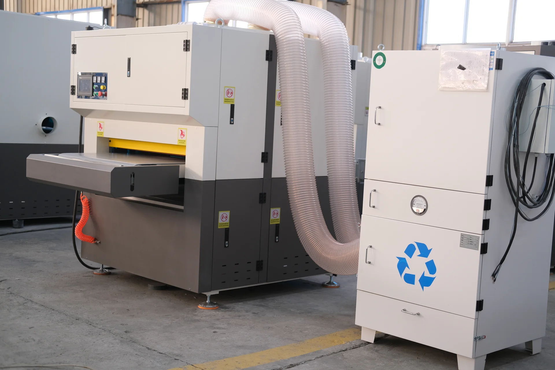 Deburring machine connected to an adjacent extraction cabinet by two flexible hoses.
