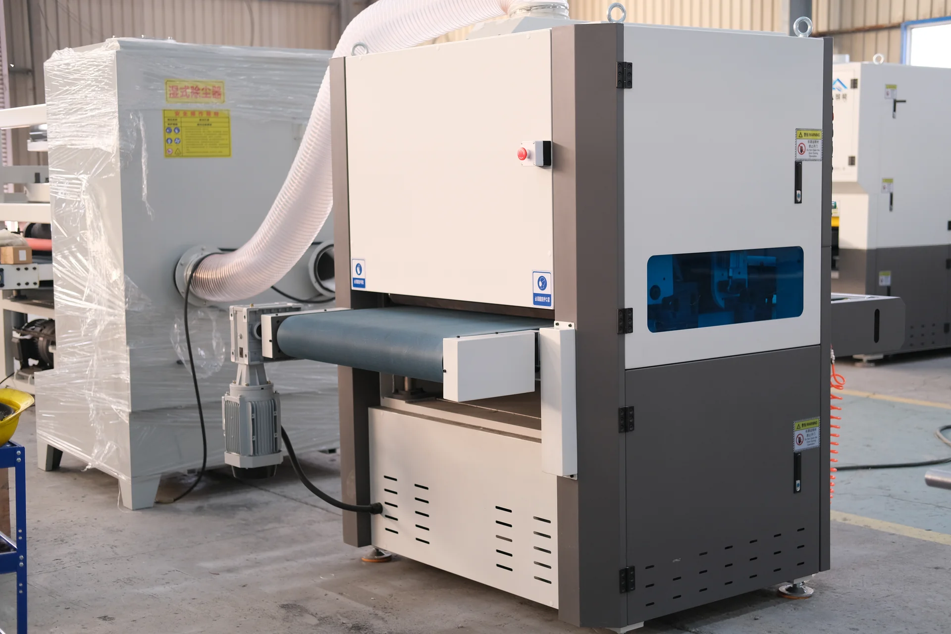 Rear three-quarter view of a deburring machine showing its conveyor drive and extraction connection.