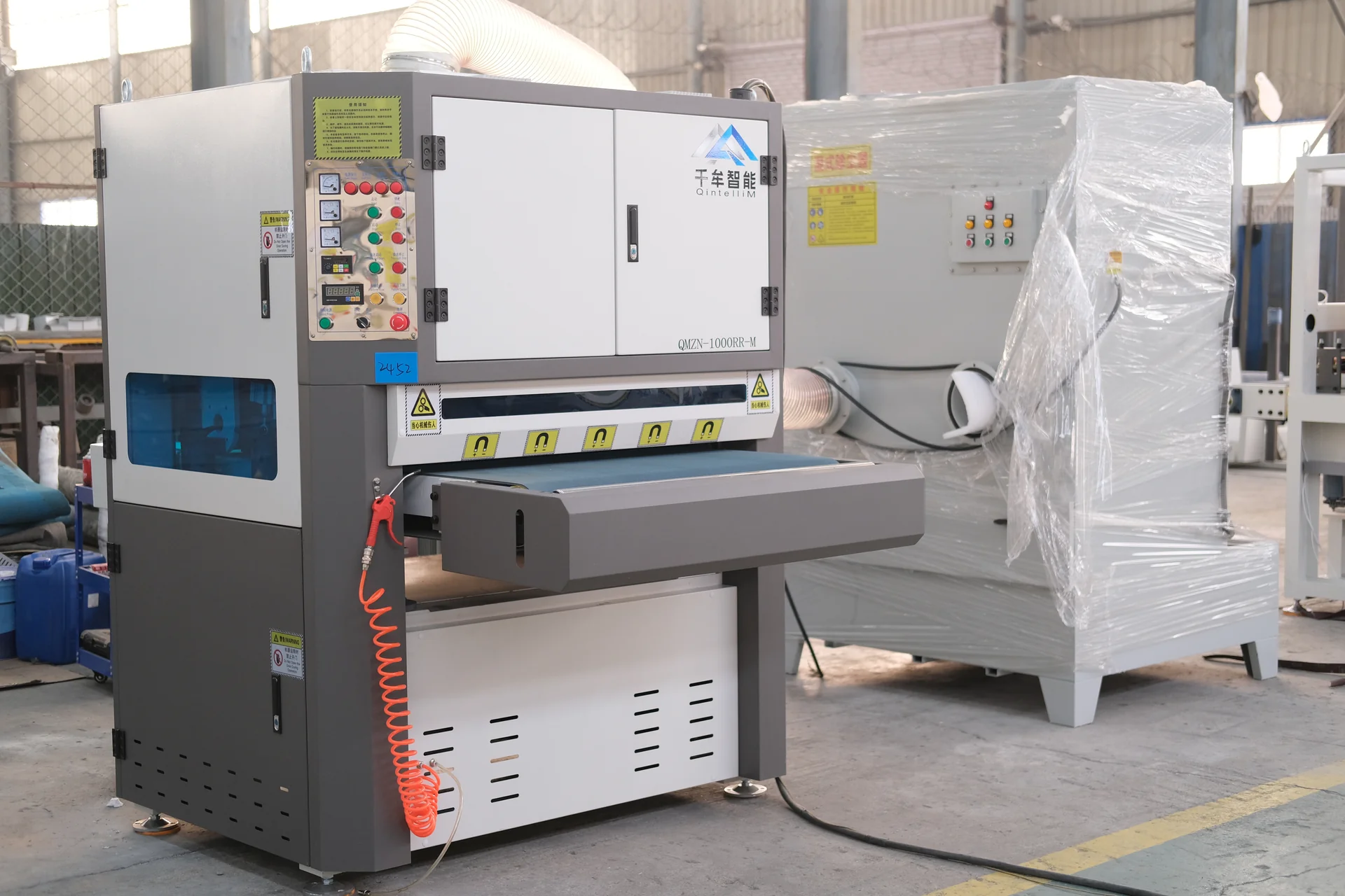 Deburring machine with a vertical control panel, front conveyor and white access doors.