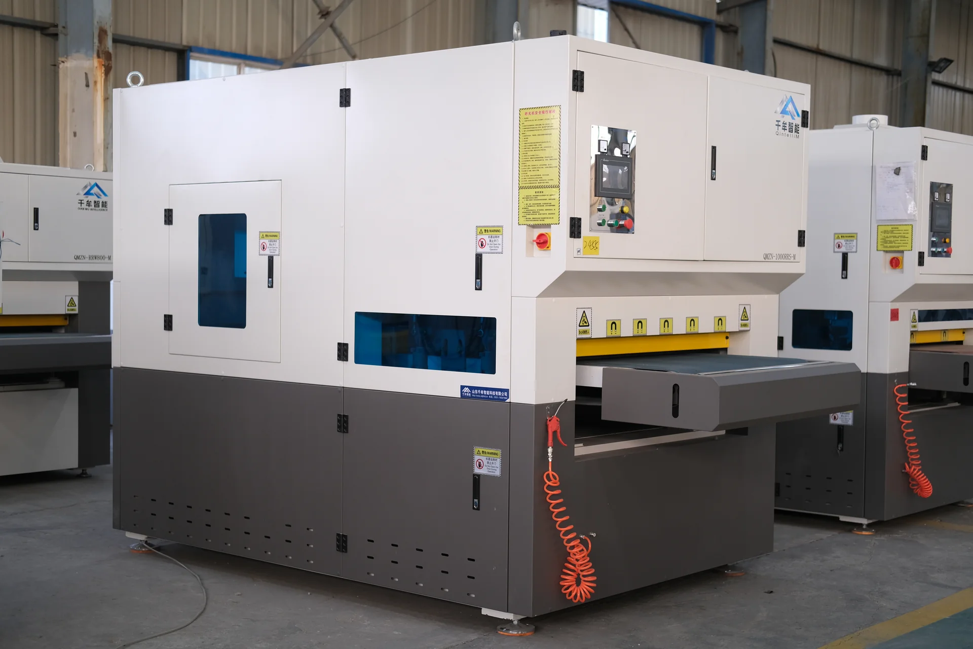 Front-left view of an enclosed deburring machine with an infeed conveyor and blue side windows.