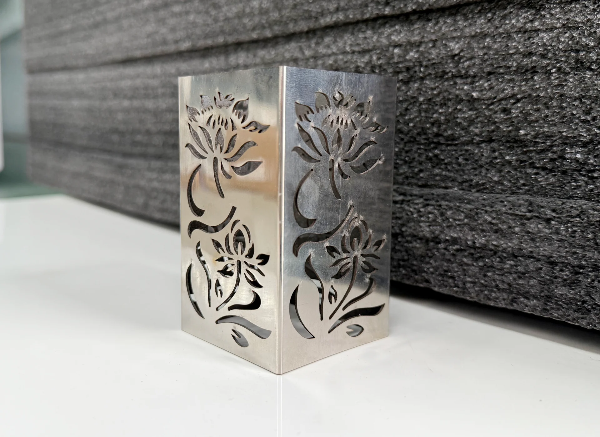 Bent metal panel with floral cutouts across two adjoining faces