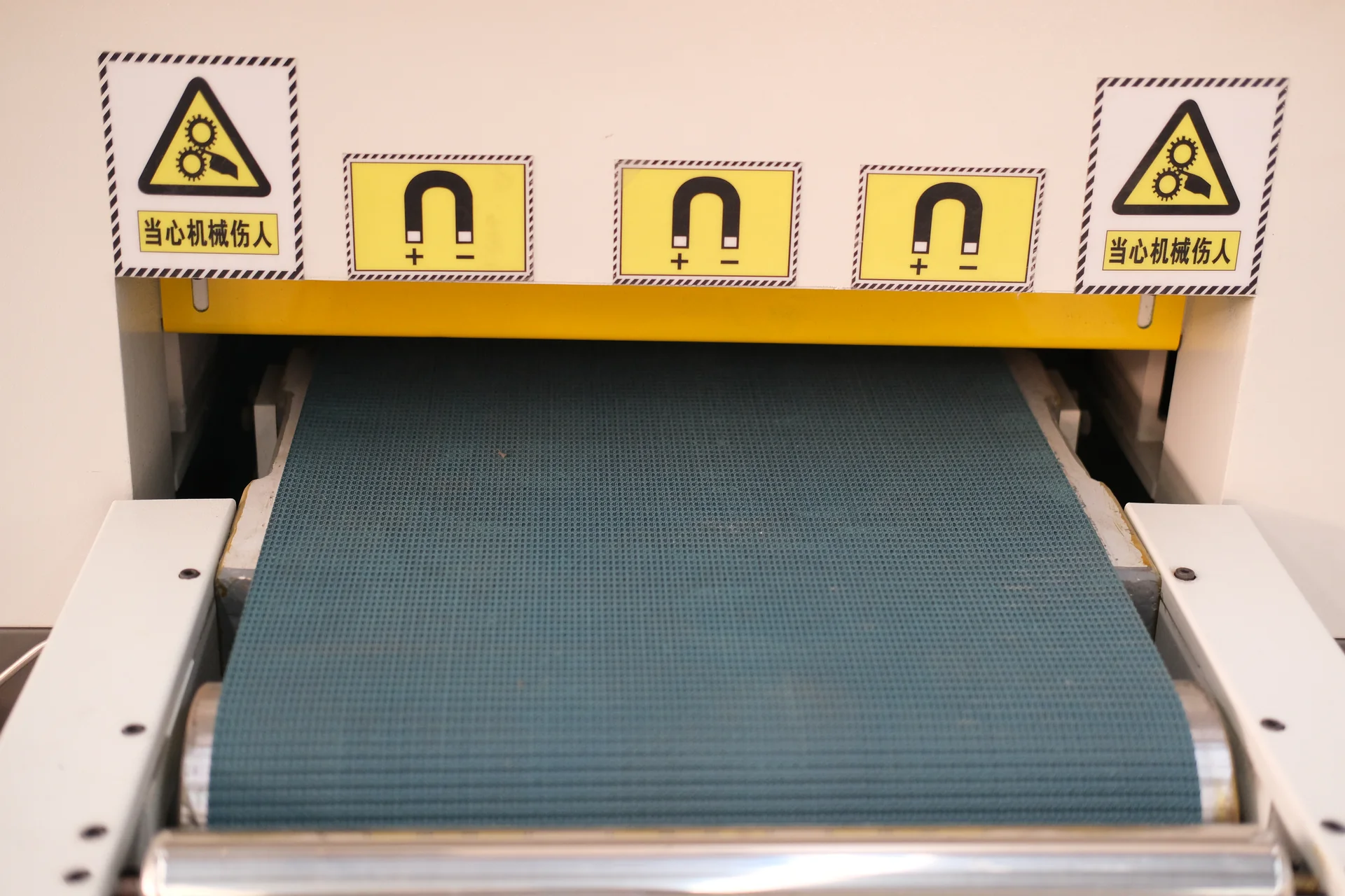 Green infeed conveyor below a yellow guard and mechanical-hazard warning labels.