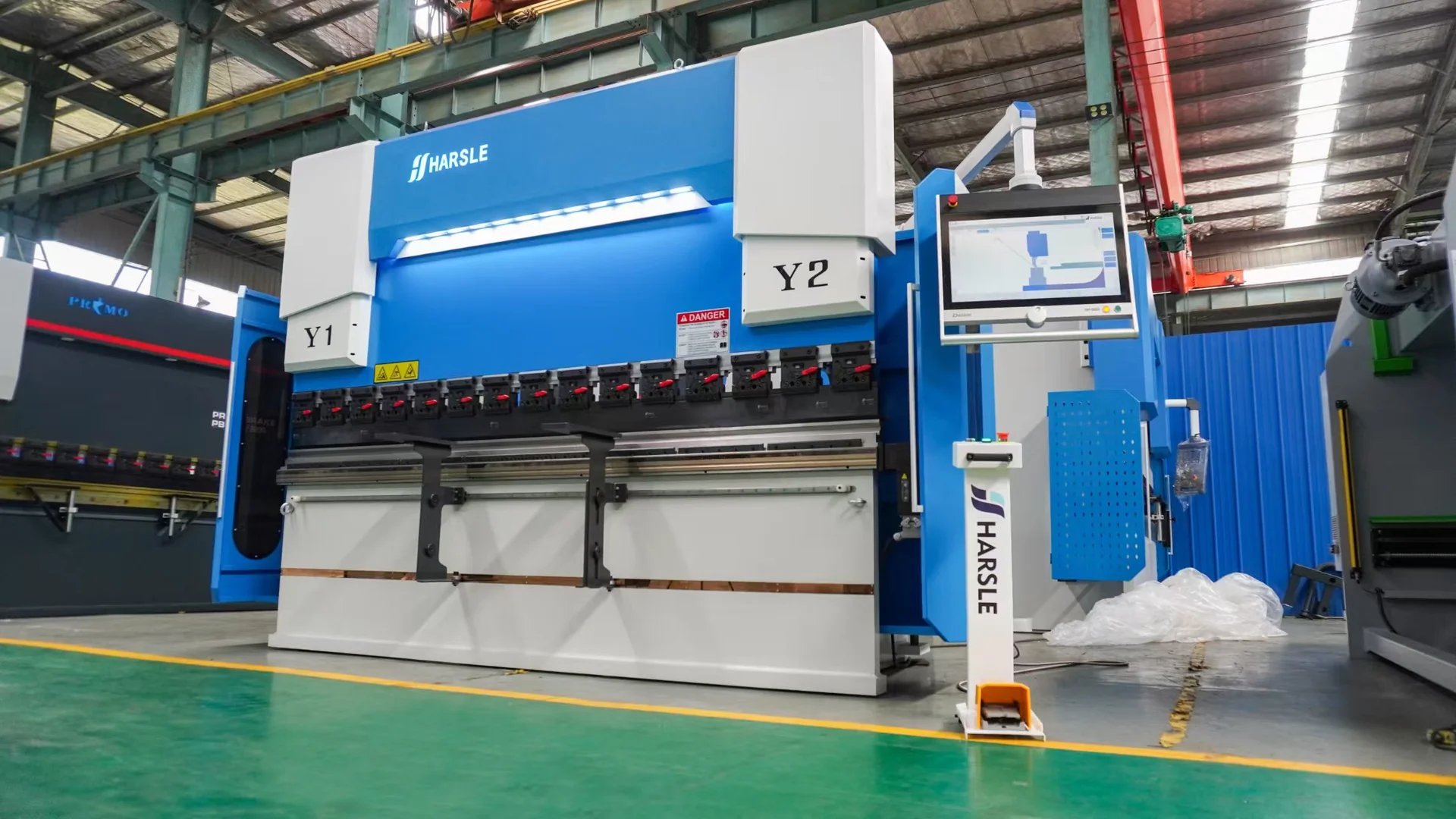 Blue and white HARSLE CNC press brake with a side-mounted controller in a workshop.