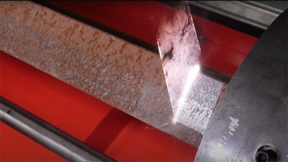 Laser cleaning removes rust from a steel workpiece, showing rusty and cleaned regions beside the active scan