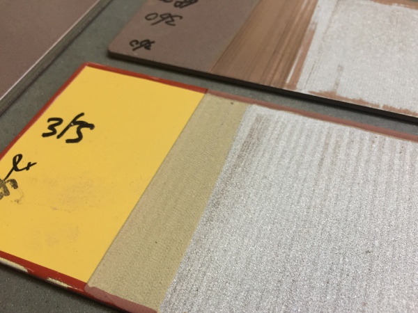 Laser paint-removal test panels with retained yellow coating and exposed underlying surface in adjacent areas