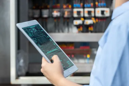 A technician using a tablet beside an electrical control cabinet