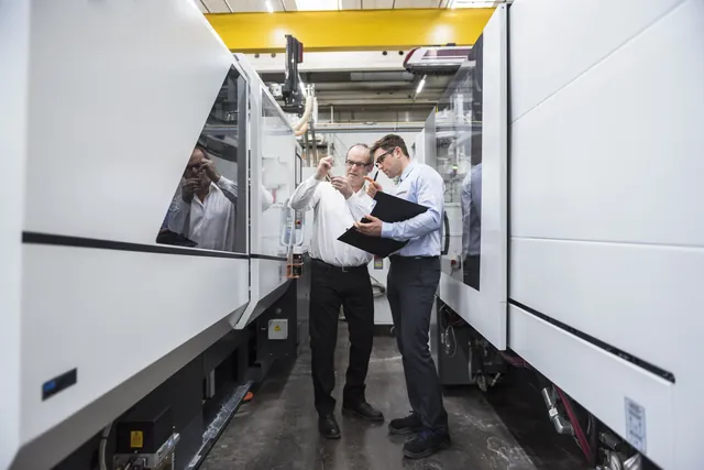 Engineers examining a component beside industrial machinery