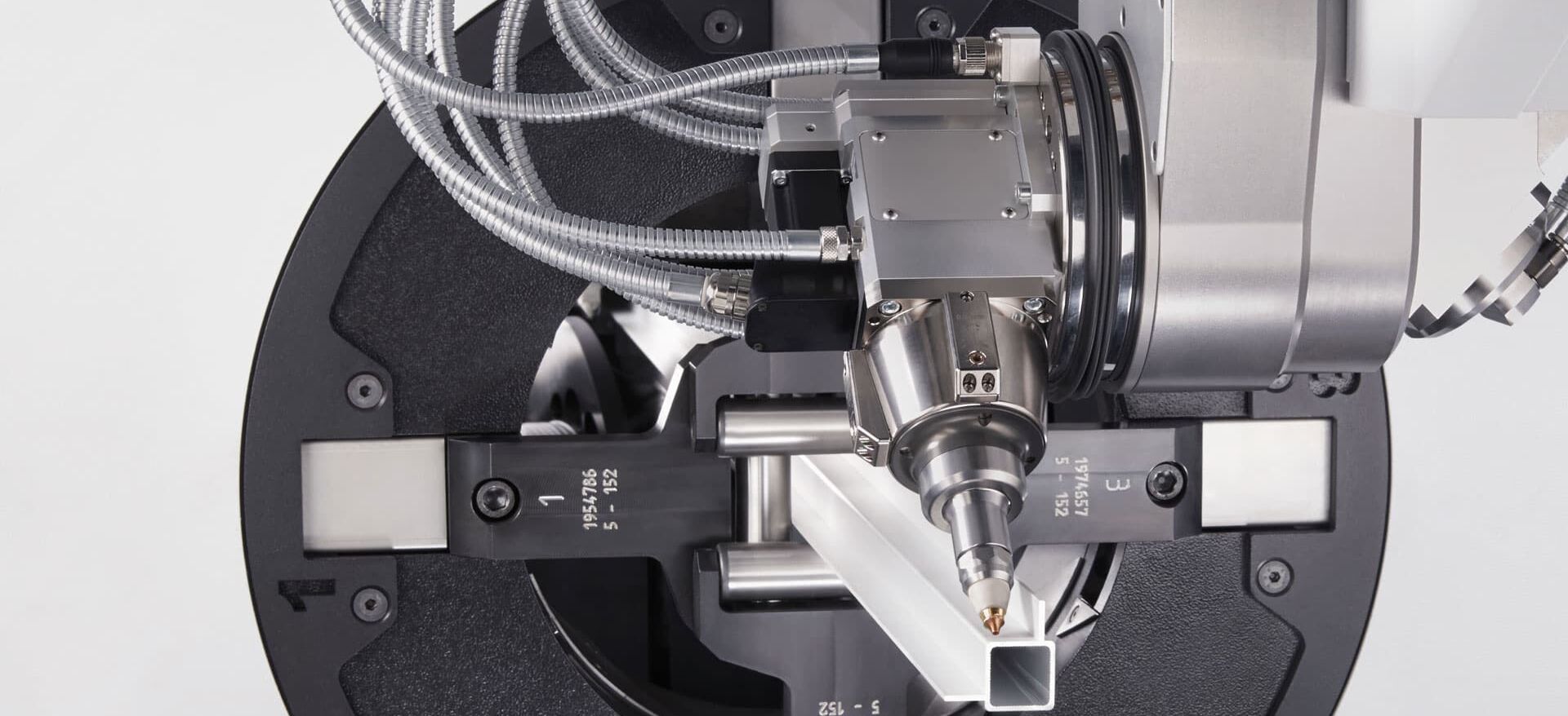 Third-party photograph of a square tube held inside a rotary chuck with the laser head near its open end