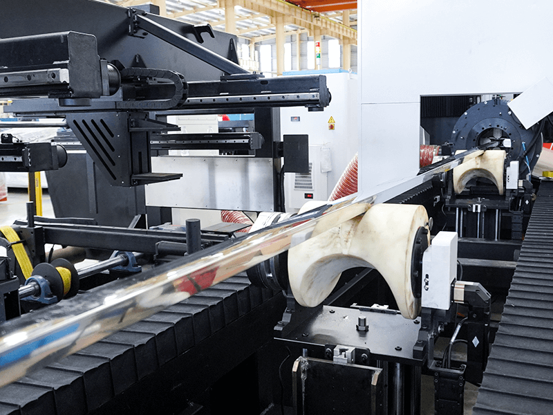 Third-party photograph of a long round tube resting on shaped auxiliary support rollers along a laser machine bed