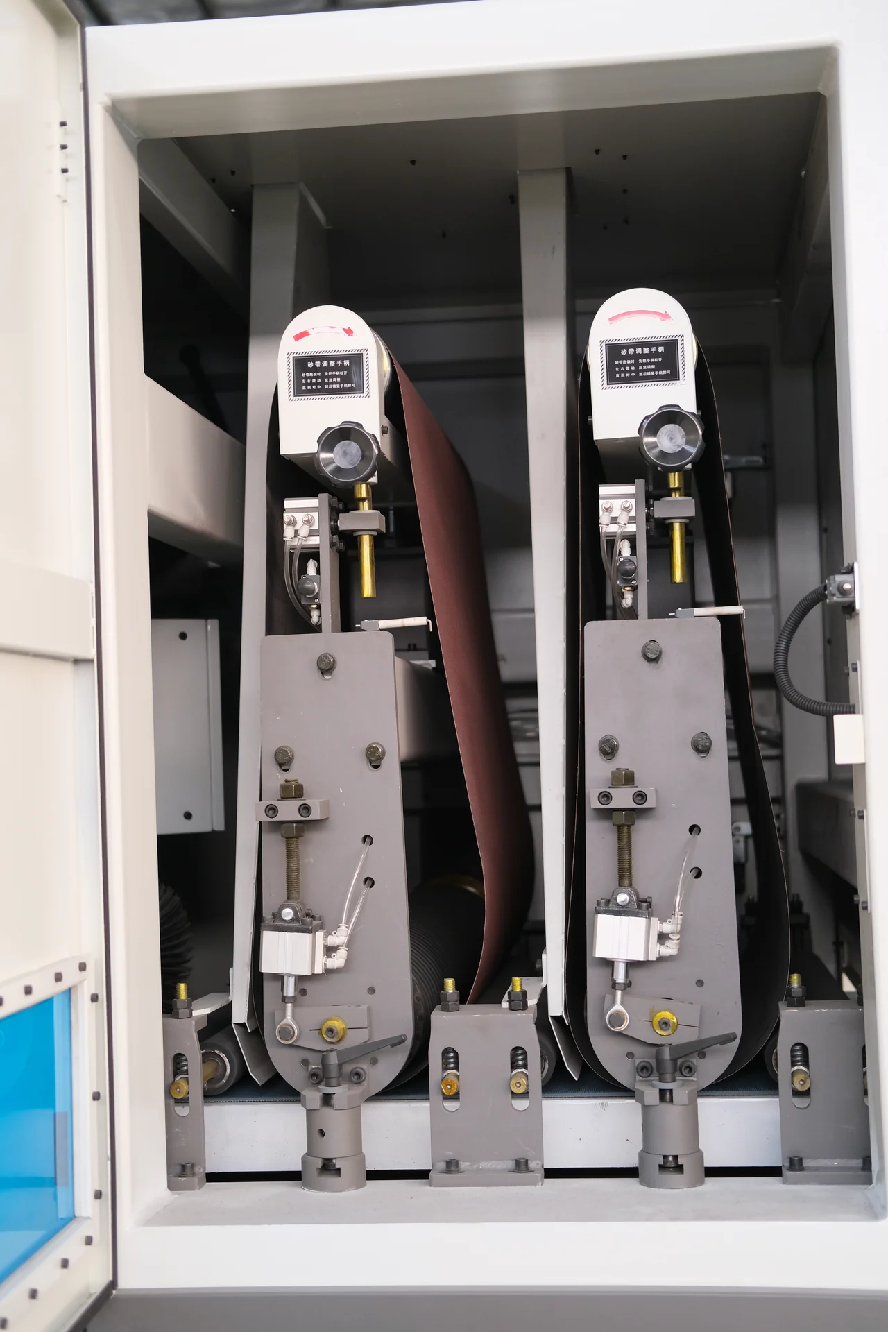 Two wide abrasive belt assemblies inside an open side compartment.